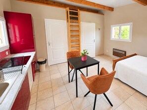 A compact room with a bed, a table, a chair, a red appliance, and a window.