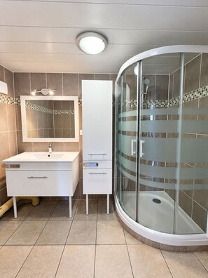 A modern bathroom with a white vanity, a glass shower enclosure, and a tiled floor.