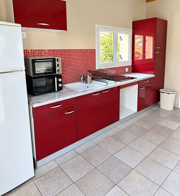 A kitchen with red cabinets, a white refrigerator, a microwave, and a window with a view of greenery.