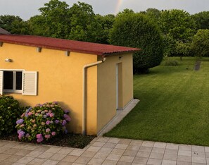 A yellow building with a red roof, a small garden with hydrangea flowers, and a grassy lawn.
