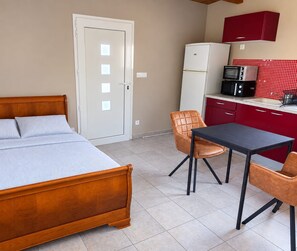 A bedroom with a wooden bed, a small table, and two chairs. There is a kitchenette with a microwave and a refrigerator.
