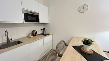Een moderne keuken met witte kastjes, een roestvrijstalen spoelbak en een magnetron. Er staat een houten eettafel met een potplant erop.