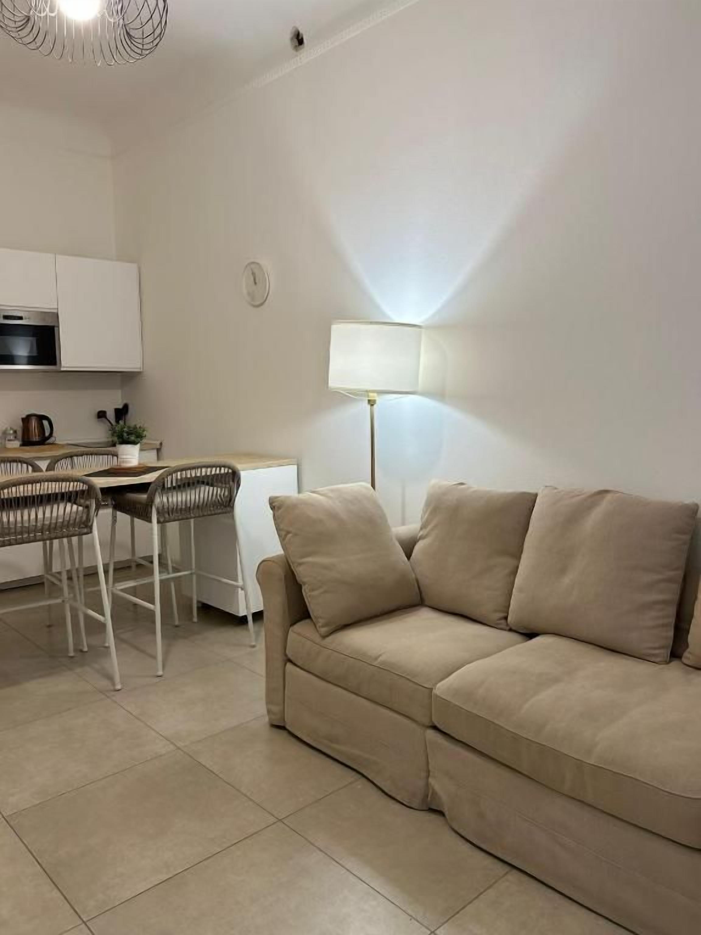 Een woonkamer met een bank, een eettafel met stoelen, een lamp en een keuken met kasten en apparatuur.