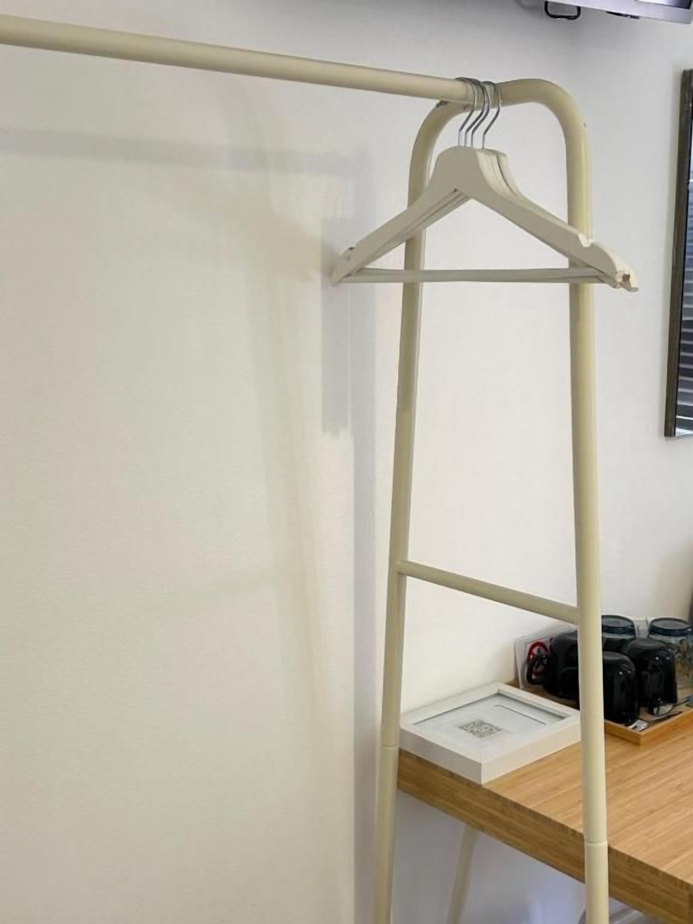 Un portant à vêtements en métal avec un cintre, une étagère sur laquelle se trouve un petit objet, et une surface en bois avec des objets noirs.