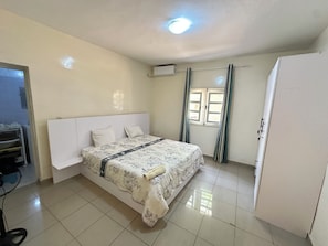 Un dormitorio con cama, armario, ventana con cortinas y equipo de aire acondicionado.
