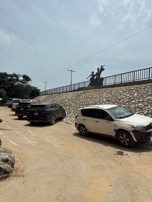 Un estacionamiento con varios autos, un muro de piedra y una estatua en la parte superior.