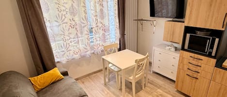 Un espacio habitable compacto con sofá, mesa de comedor, televisor montado en la pared y kitchenette con microondas.