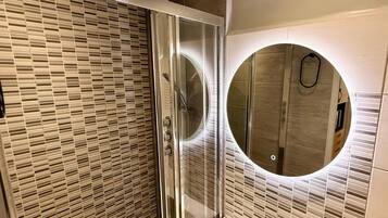 A modern bathroom with a glass shower enclosure, a round mirror, and a tiled wall.