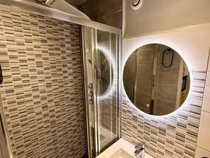 A modern bathroom with a glass shower enclosure, a round mirror, and a tiled wall. - Apartment for two Guest, Mont-dore (Mont-Dore)