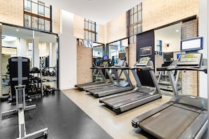 Academia com esteiras, aparelhos de musculação e espelhos nas paredes.