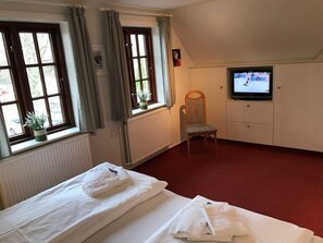 Ein Hotelzimmer mit zwei Betten, einem Fernseher, einem Sessel und einem Fenster mit Vorhängen.