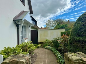A narrow brick pathway leading to a white building with a dark door and a small window. - Hansen Nieblum - Holiday Apartment 1 (Nieblum)