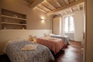 Une chambre d’hôtel avec deux lits, une étagère ornée d’objets décoratifs, un lampadaire fixé au mur et une fenêtre avec des rideaux.