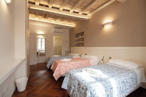Une chambre d’hôtel avec deux lits, un plancher en bois, une étagère intégrée et une fenêtre avec des rideaux.