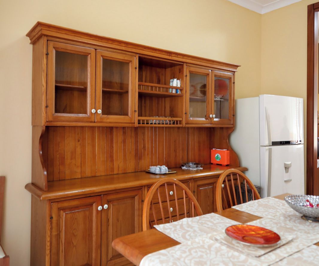 A wooden cabinet with glass doors, a white refrigerator, and a dining table with chairs.