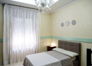 A bedroom with a bed, a nightstand, a chandelier, and a window with curtains. - Maureen Holiday House (napoli)