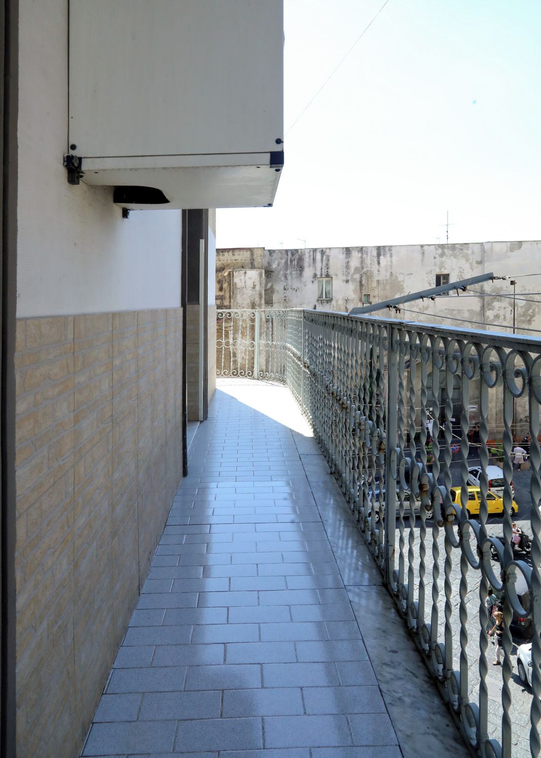 A narrow outdoor corridor with a metal railing on one side and a brick wall on the other.