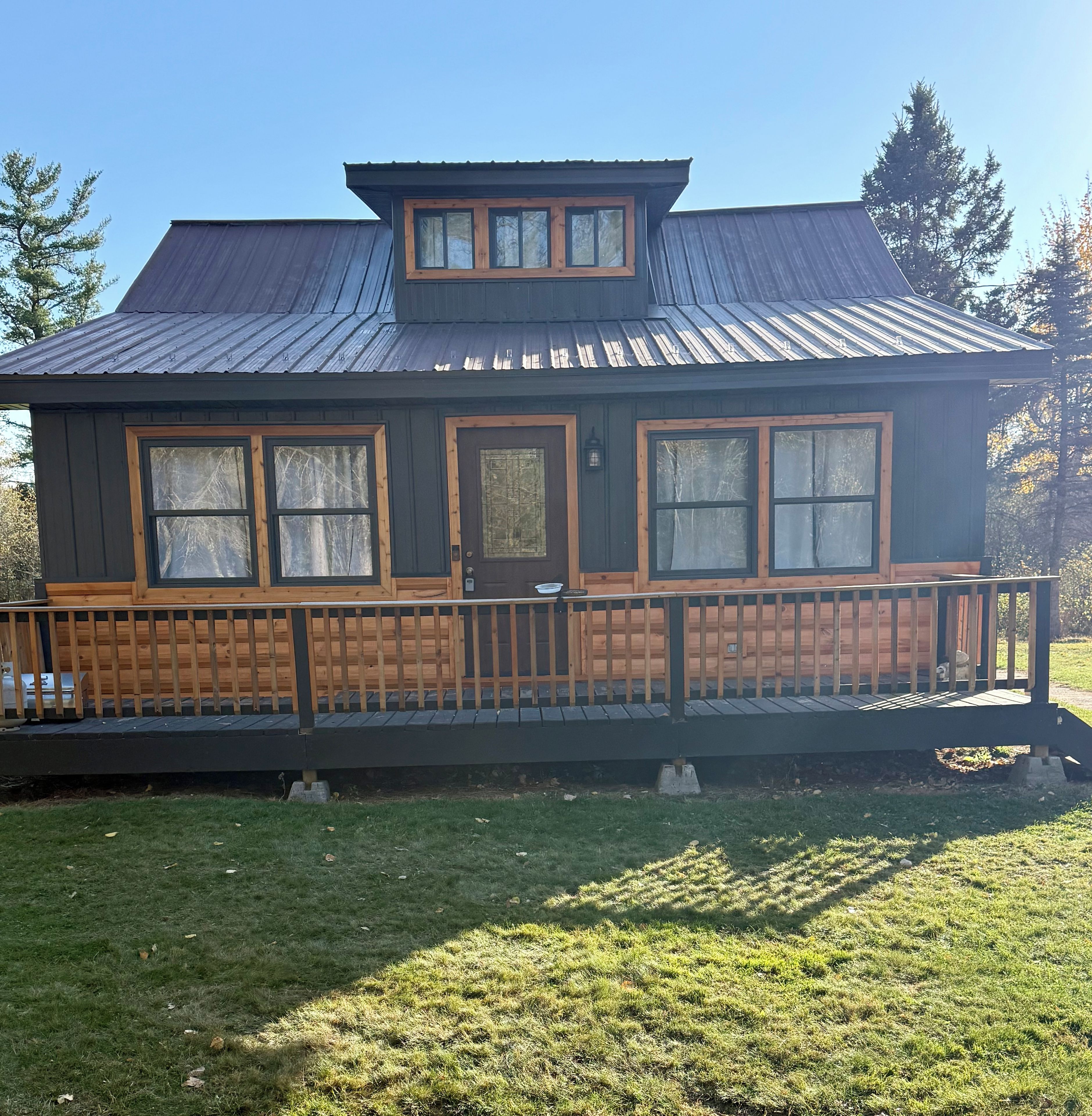 A two-story cabin with a metal roof, wooden deck, and a fenced front yard.
