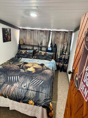 Une chambre à coucher avec un lit orné d’une couette à motifs d’ours, une tête de lit en bois, une table de chevet avec une lampe et une porte décorée d’un motif d’ours.