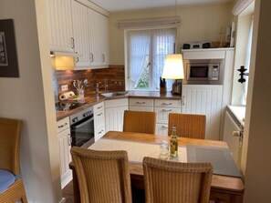 A compact kitchen with white cabinetry, a dining table with chairs, and a microwave. - 8b in the Building on Neuer Weg (Wrixum)