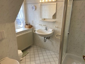Une salle de bain avec un lavabo blanc, un miroir, des toilettes et un espace douche.