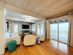 A spacious living area with a wooden ceiling, a television, a sofa, a coffee table, and a view of the outdoors through large sliding doors. - Beach Barnacle on Sunset Beach (Treasure Island)