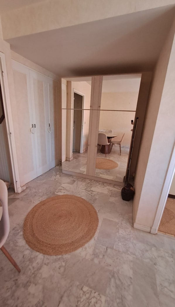 A hallway with a round woven rug, a dining area with chairs and a table, and a white door with a handle. - Vrbo Property (Cannes)