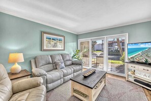 A living room with a grey sofa, a coffee table, and a TV on a wooden stand. - Dans Florida Condos Ocean Sands at Runaway Bay (Bradenton Beach)