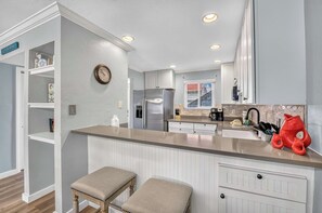 A kitchen with white cabinetry, a stainless steel refrigerator, a built-in oven, and a large island with stools. - Dans Florida Condos Ocean Sands at Runaway Bay (Bradenton Beach)