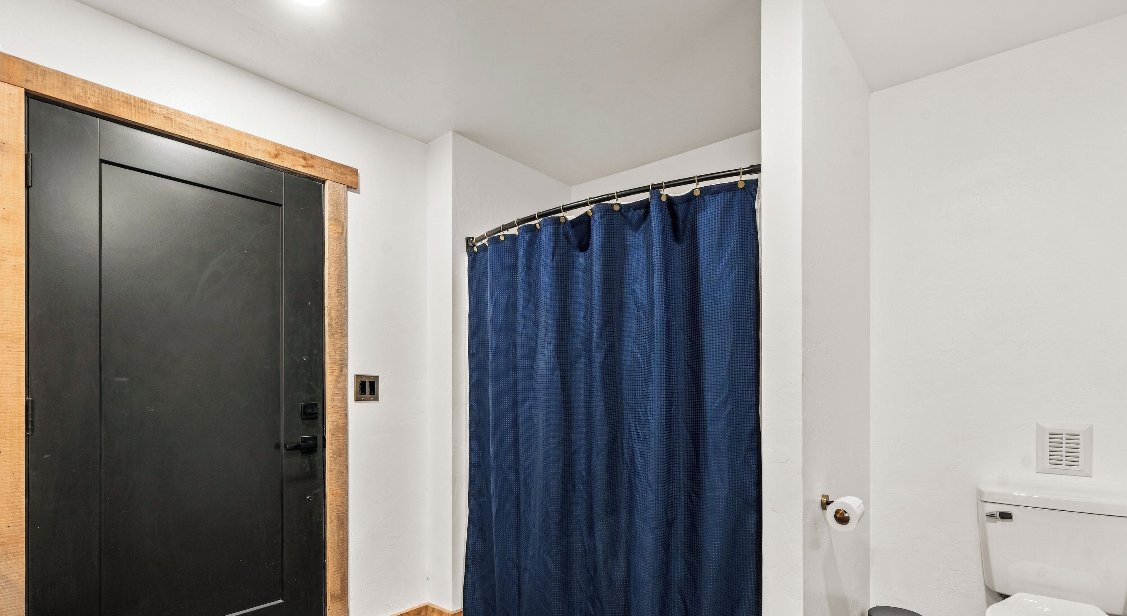 A bathroom with a black door, a blue shower curtain, and a white toilet.