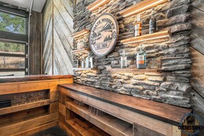 Un rústico espacio de bar con pared de piedra, estantes de madera y un banco.