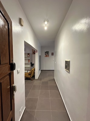 A hallway with a wooden door, a ceiling light, a chair, and framed pictures on the walls. - Vrbo Property (Dakar)