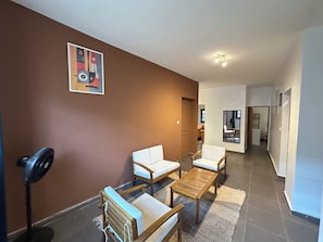 A living room with a brown wall, a ceiling fan, a sofa, a coffee table, and a rug. - Vrbo Property (Dakar)
