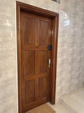 A wooden door with a keypad lock, set in a hallway with tiled walls and a carpeted entrance. - Vrbo Property (Dakar)