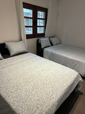 A room with two beds, a window with curtains, and a view of buildings outside. - Vrbo Property (Dakar)