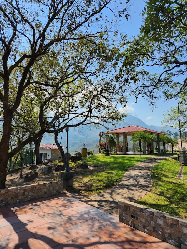 A gazebo with a red roof, surrounded by a stone wall and a paved walkway.
