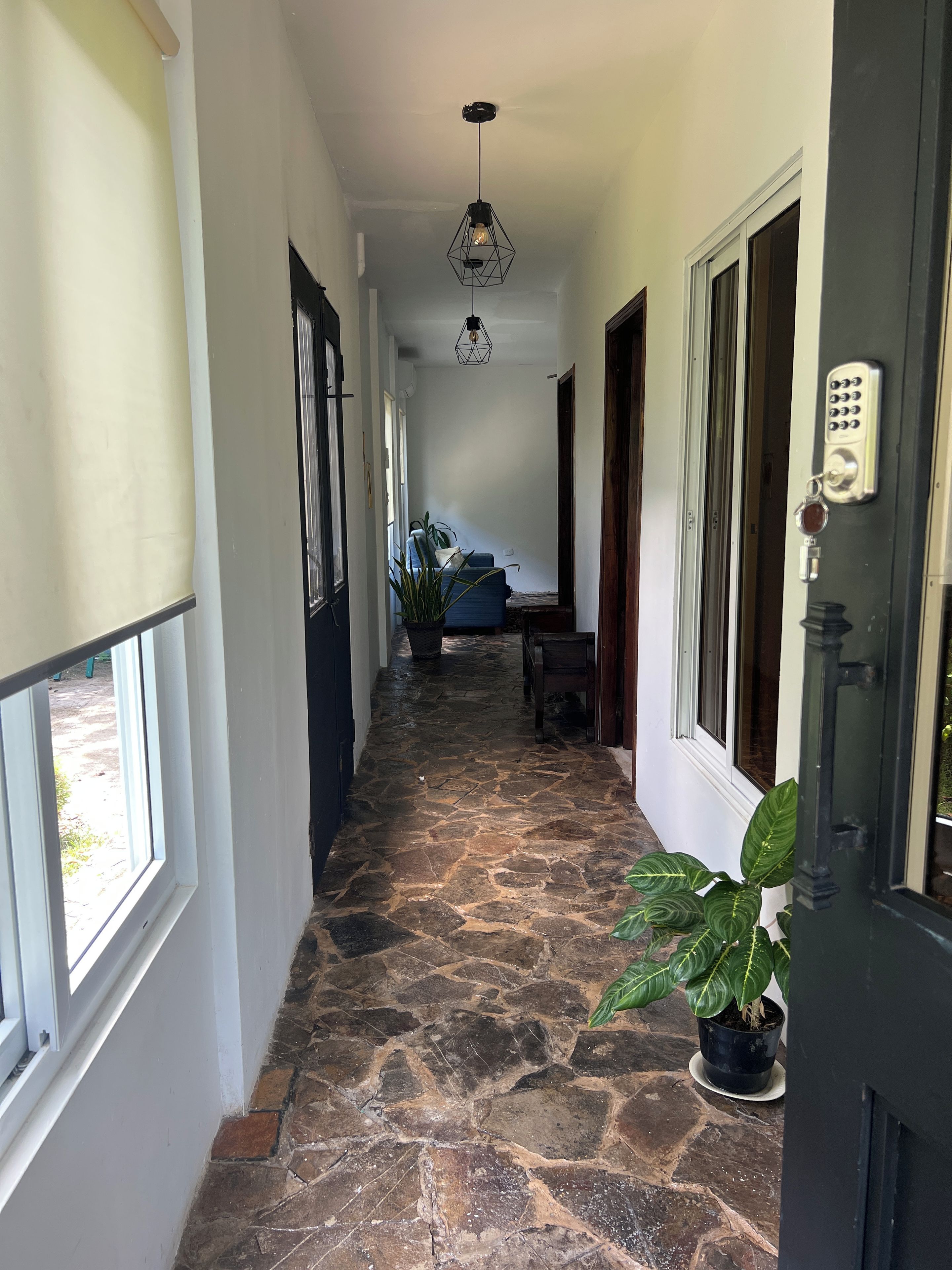 A hallway with stone flooring, a door with a keypad lock, and a hanging light fixture.