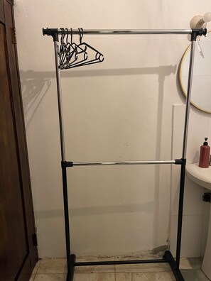 A bathroom with a metal rack for hanging clothes, a sink, and a mirror.
