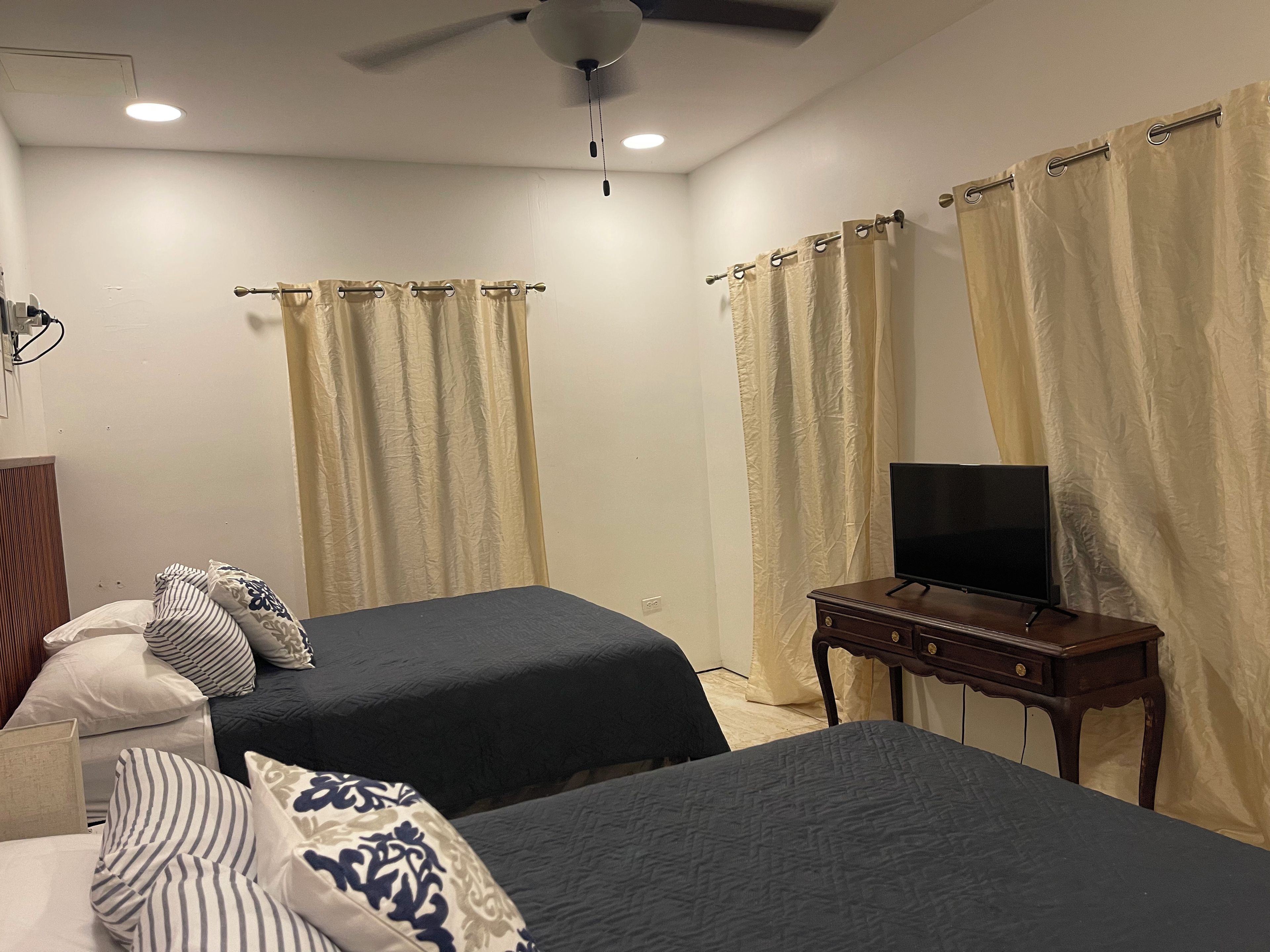 A hotel room with two beds, a television on a wooden table, and curtains on the windows.
