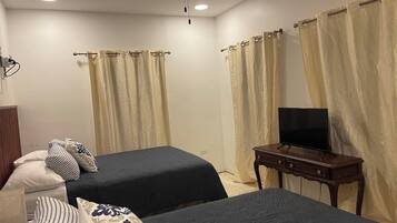 A hotel room with two beds, a television on a wooden table, and curtains on the windows.