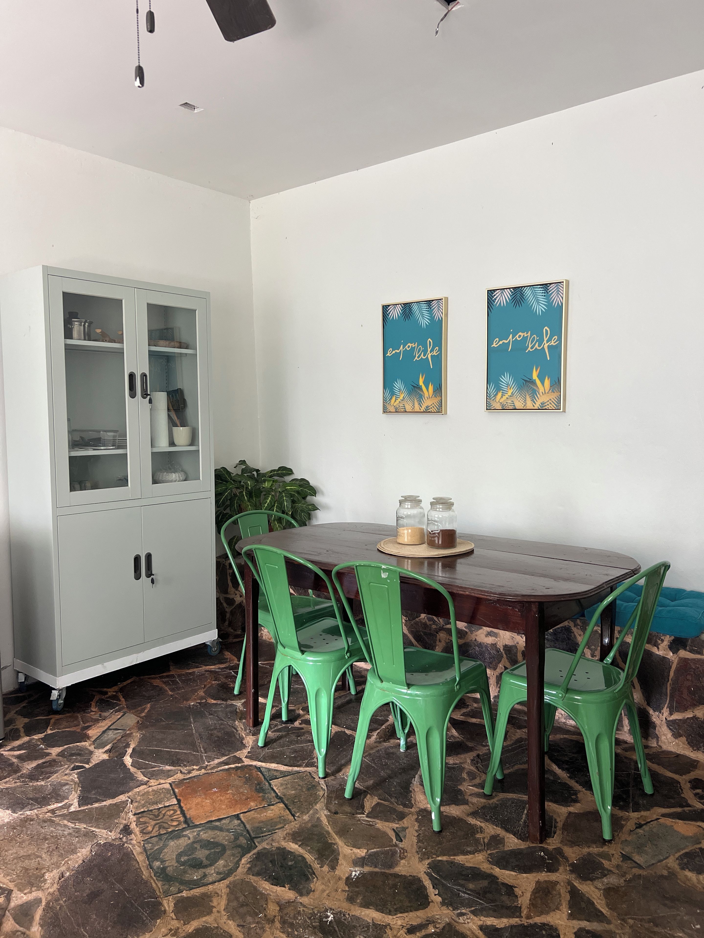 A dining area with a wooden table, green chairs, a cabinet, and two wall art pieces.