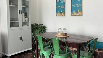 A dining area with a wooden table, green chairs, a cabinet, and two wall art pieces.