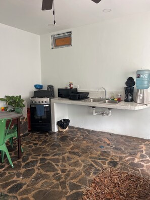 A kitchen with a stone floor, a sink, a stove, a water dispenser, and a trash bin. - Cozy 1-bedroom apartment in tranquil Departamento de Santa Bárbara with AC (Departamento de Santa Bárbara)