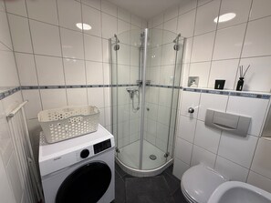 Moderni kylpyhuone, jossa on lasiseinällä varustettu suihku, pesukone ja wc.