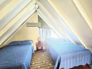 Ein Zimmer mit zwei Betten, einem fensterbepften Fenster und einem kleinen Tisch mit Lampe.