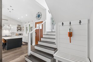 A modern kitchen with a central island, a staircase with a railing, and a wall-mounted key rack. - Modern Coastal Cottage|Hot Tub|Privacy|BEST Locati (Kennebunk)