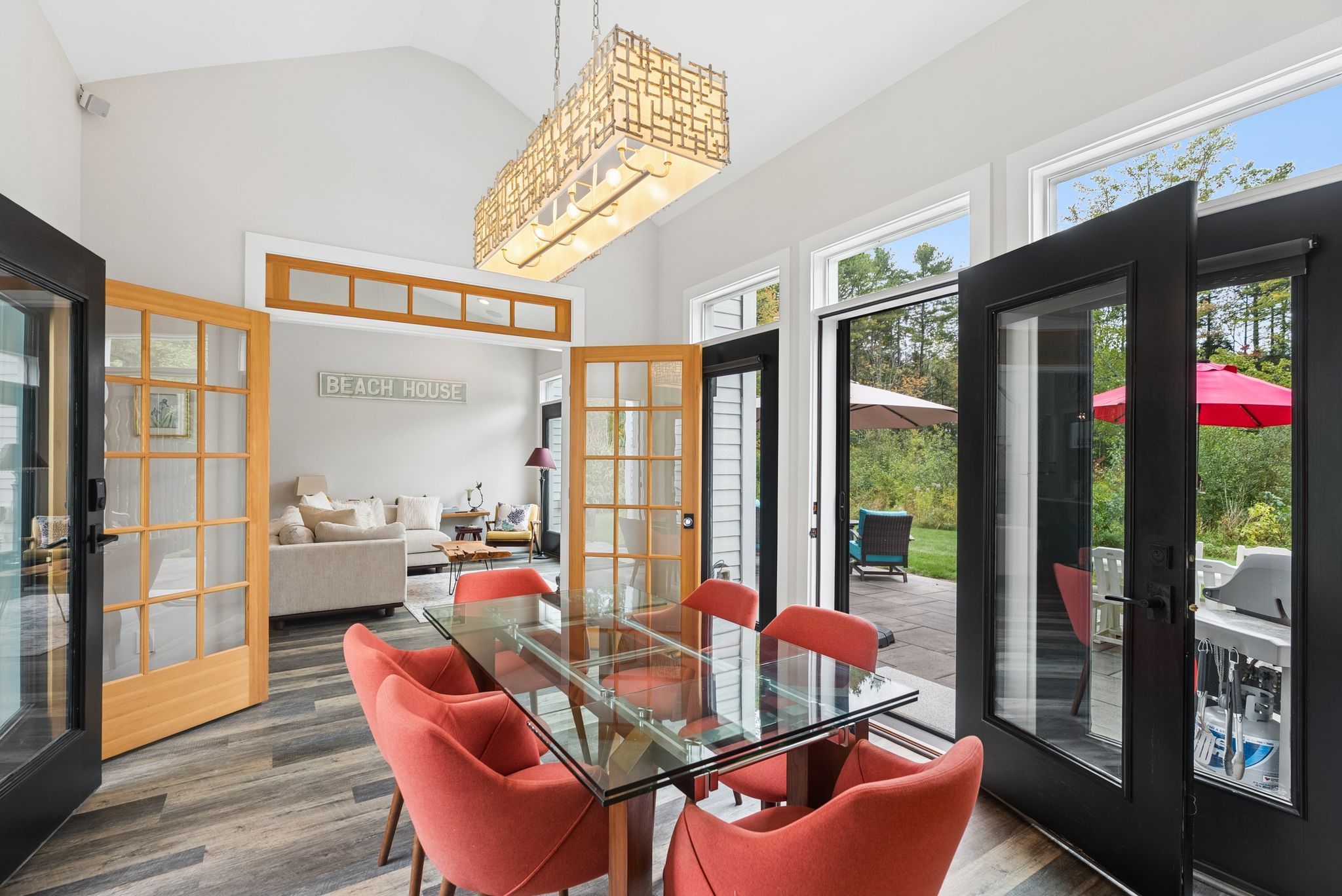 Ein modernes Interieur mit einem Glastisch, roten Stühlen und einem Schild mit der Aufschrift 'BEACH HOUSE' an der Wand.
