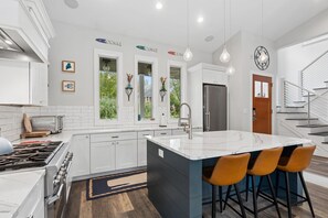 Una cocina moderna con armarios blancos, una isla grande con taburetes de bar y un refrigerador de acero inoxidable.