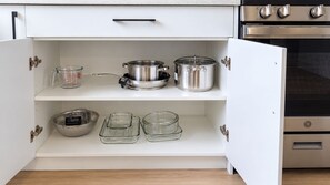 An open kitchen cabinet with stainless steel cookware, a measuring cup, and glass containers. - 3 BR Home-7 minutes from West Edmonton Mall (Edmonton)