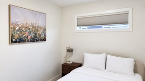 A bedroom with a bed, a nightstand, a lamp, a window with blinds, and a painting on the wall. - 3 BR Home-7 minutes from West Edmonton Mall (Edmonton)
